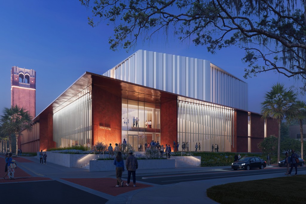 A modern building at dusk with large windows, people outside, and a lit brick tower in the background.